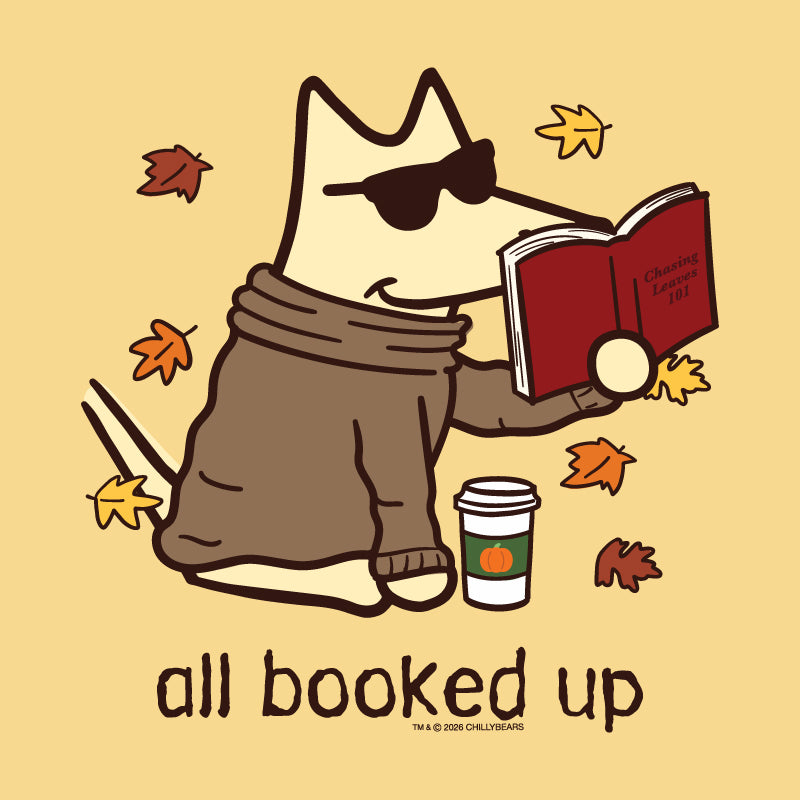 A stylized cartoon dog wearing sunglasses and a brown sweater sits reading a red book, with autumn leaves around it and the text 'all booked up' below. The artwork is on a warm beige background.