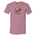 A heathered dusty rose short-sleeve t-shirt with a cartoon graphic of a dog wearing a trench coat and holding a red book, surrounded by autumn leaves, with the text 'all booked up' printed below.