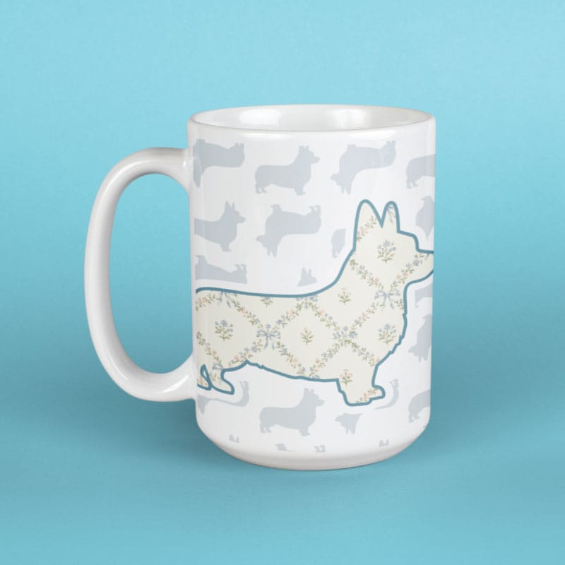 A white ceramic mug featuring a Corgi silhouette filled with a floral pattern in beige and blue, set against a background of light gray Corgi silhouettes. The mug is photographed on a solid light blue background.
