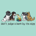 A graphic design featuring cartoon dogs of various breeds wearing sunglasses, with a small dog standing on a stack of books. Below them is the text 'don't judge a bark by its size' in black lowercase letters, all set against a solid light teal background.