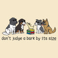 A beige graphic print featuring five cartoon dogs wearing sunglasses, with one small dog standing on a stack of colorful books. Below the illustration, the text reads 'don't judge a bark by its size' in black lowercase letters.