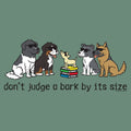 A graphic design on a muted green background featuring five cartoon dogs wearing sunglasses, with one small dog standing on a stack of books. Below the illustration, the text reads 'don't judge a bark by its size'.