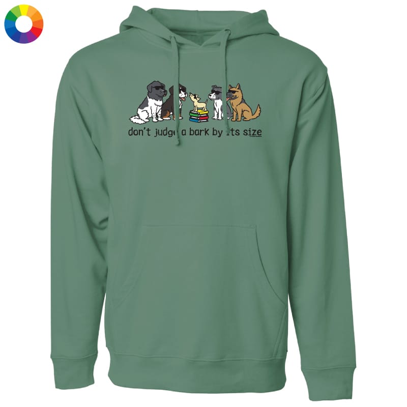 A sage green pullover hoodie with a graphic of several dog breeds sitting on a stack of books and the text 'don't judge a bark by its size' printed on the chest. A small multicolor color wheel icon is in the top-left corner.