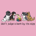 A pink graphic print featuring cartoon dogs of various sizes sitting around a small stack of books, with the text 'don't judge a bark by its size' underneath. A small '© www.