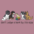A graphic print featuring cartoon dogs of various sizes and breeds sitting around a small stack of books, with the text 'don't judge a bark by its size' below. The background is a solid dusty mauve color.