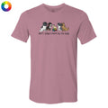 A dusty rose short-sleeve t-shirt with a graphic of four dogs of different sizes sitting together with a small rainbow-colored object, and the text 'don't judge a bark by its size' printed below. A small multicolor color wheel icon is in the top-left corner.