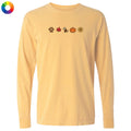 A pale yellow long-sleeve t-shirt with a row of small autumn-themed icons printed across the chest, including a paw print, maple leaf, raccoon, pumpkin, and sun. A multicolor color wheel icon is visible in the top-left corner.
