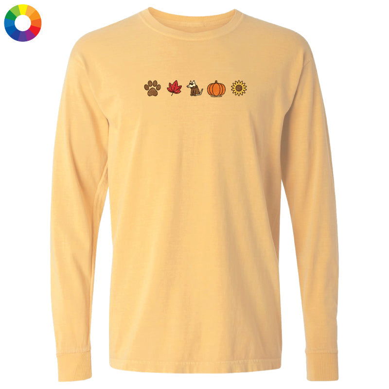 A pale yellow long-sleeve t-shirt with a row of small autumn-themed icons printed across the chest, including a paw print, maple leaf, raccoon, pumpkin, and sun. A multicolor color wheel icon is visible in the top-left corner.