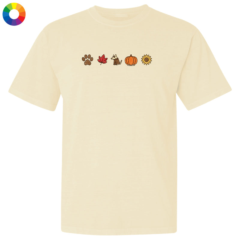 A cream-colored short-sleeve t-shirt with a horizontal row of small autumn-themed icons printed on the chest, including a paw print, maple leaf, dog, pumpkin, and sunflower. A circular multicolor color wheel icon is visible in the top-left corner.