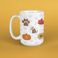 A white ceramic mug with a handle, decorated with an autumn-themed pattern featuring a brown paw print, a red maple leaf, a cartoon dog in a brown coat, an orange pumpkin, a yellow sunflower, and faint pink leaves, set against a solid mustard yellow background.