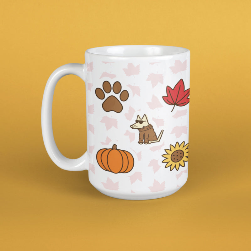 A white ceramic mug with a handle, decorated with an autumn-themed pattern featuring a brown paw print, a red maple leaf, a cartoon dog in a brown coat, an orange pumpkin, a yellow sunflower, and faint pink leaves, set against a solid mustard yellow background.