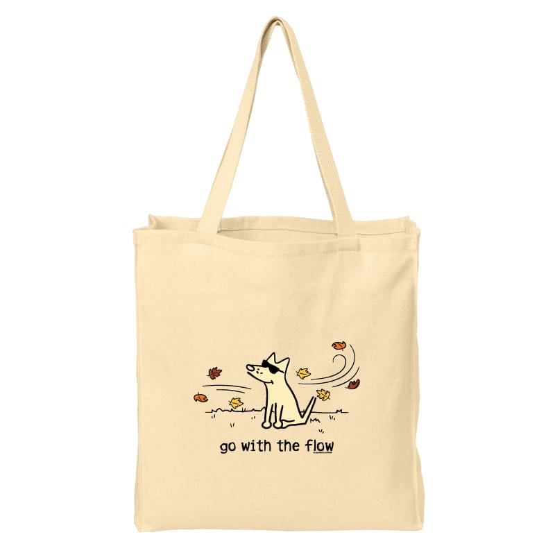 A natural beige canvas tote bag with two shoulder straps, featuring a minimalist black line art illustration of a dog surrounded by autumn leaves and the text 'go with the flow' printed on the front.