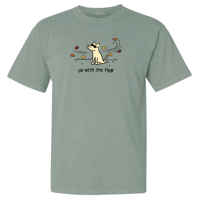 A sage green short-sleeve t-shirt with a graphic of a white dog looking up at flying leaves, with the text 'go with the flow' printed below.