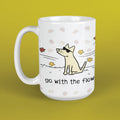 A white ceramic mug with a cartoon dog wearing sunglasses and the text 'go with the flow', decorated with light pink and yellow autumn leaves, set against a solid yellow-green background.