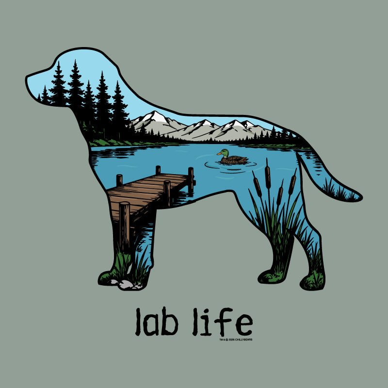 A stylized dog silhouette filled with a scenic landscape illustration of a lake, mountains, dock, trees, and a duck, with the text 'lab life' below on a muted green background.