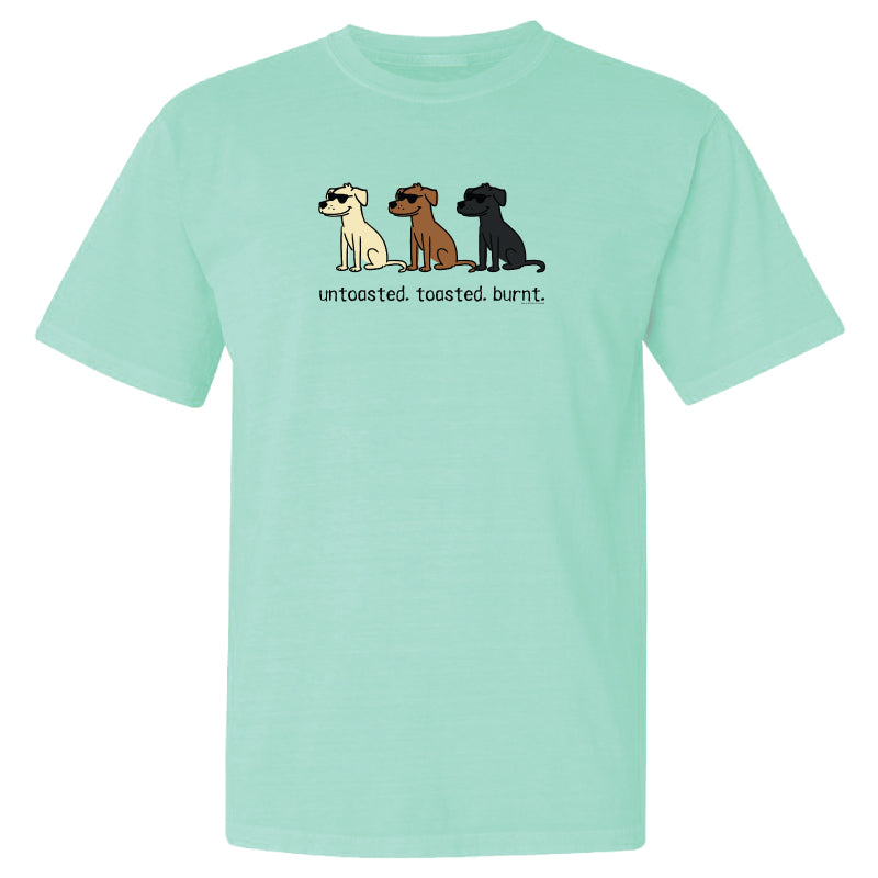 A mint green short-sleeve t-shirt with a graphic of three cartoon dogs in cream, brown, and black, with the text 'untoasted. toasted.