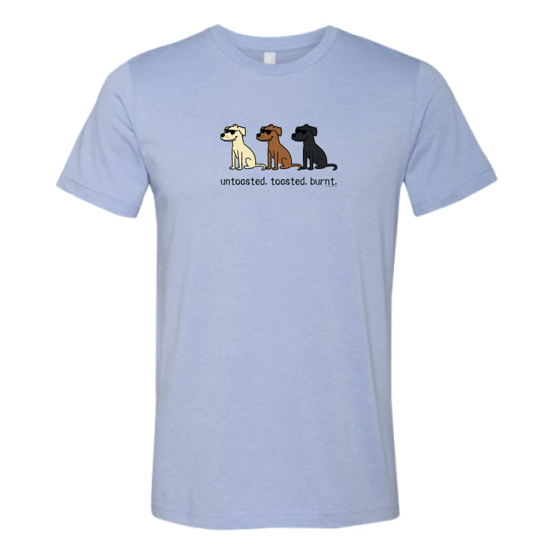 A light blue heather crewneck t-shirt featuring a graphic of three cartoon dogs in white, brown, and black, with the text 'uncoated, toasted, burnt.' printed below them.