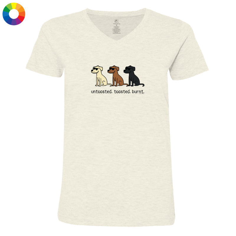 A women's short-sleeve V-neck t-shirt in a light heathered cream color, featuring a graphic of three dogs (Beagle, Labrador, and Rottweiler) with the text 'untoasted, toasted, burnt.' underneath.