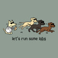 A cartoon-style graphic on a muted sage green background showing four dogs running across grass, including one dog dressed as a doctor in a white coat and sunglasses. Below the illustration, the text reads 'let's run some labs' with a small 'Y'all Can Do Everything' mark at the lower right.