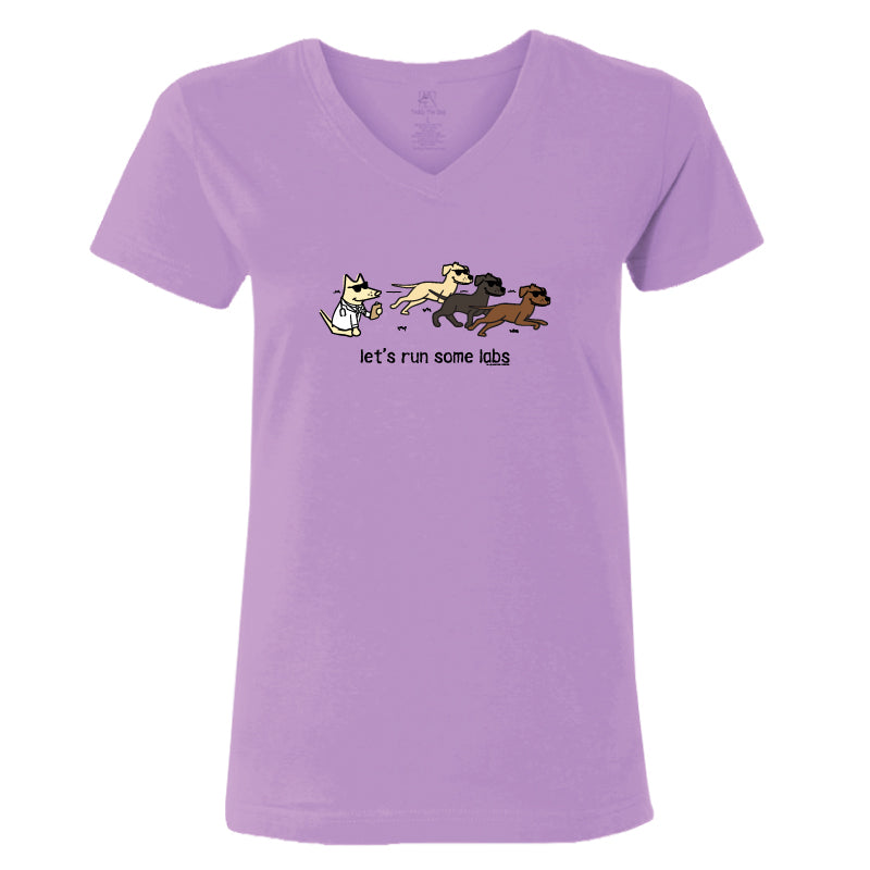 A light purple V-neck t-shirt featuring a cartoon graphic of a white cat chasing three running Labs, with the text 'let's run some labs' printed below.