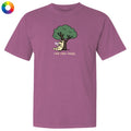 A mauve purple short-sleeve t-shirt with a cartoon graphic of a cat under a green tree reading 'read, relax, repeat.' on the chest, shown on a plain white background with a small multicolor color wheel icon in the top-left corner.