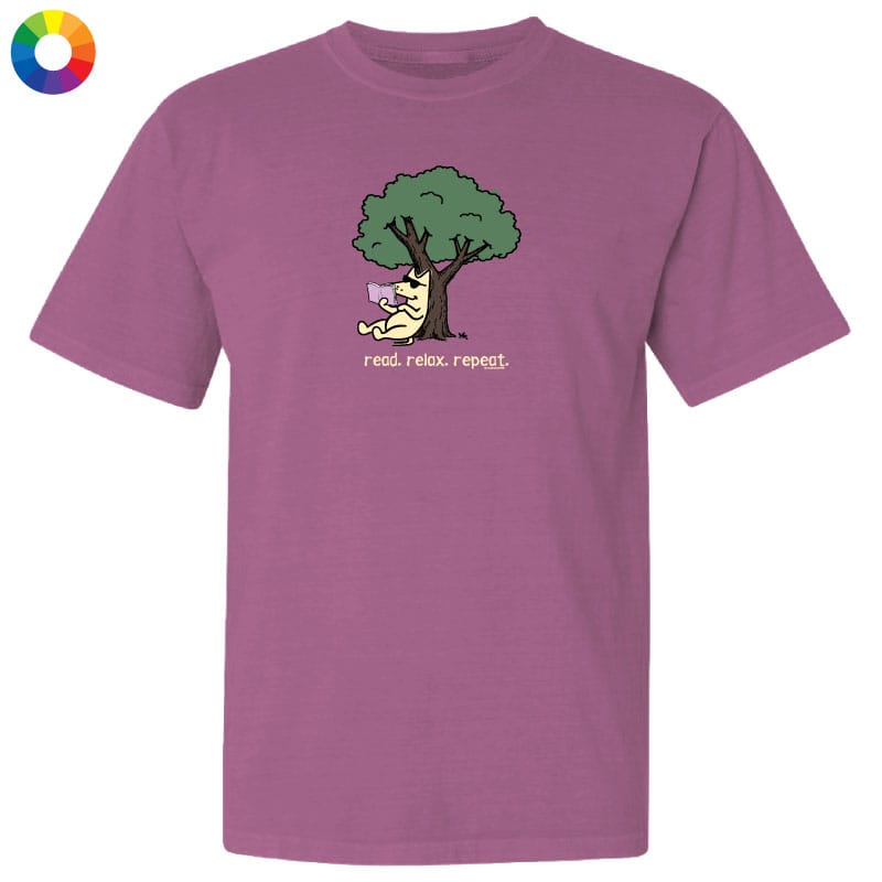 A mauve purple short-sleeve t-shirt with a cartoon graphic of a cat under a green tree reading 'read, relax, repeat.' on the chest, shown on a plain white background with a small multicolor color wheel icon in the top-left corner.