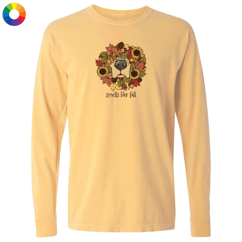 A pale yellow long-sleeve t-shirt with a graphic of a dog's face surrounded by autumn leaves and sunflowers, with the text 'smells like fall' printed below. The shirt is displayed on a solid white background, with a small multicolor color wheel icon in the top-left corner.
