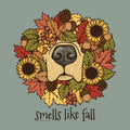 A circular autumn wreath illustration featuring a dog nose at the center, surrounded by sunflowers, fall leaves, acorns, pinecones, and berries, with the text 'smells like fall' below on a muted blue-gray background.