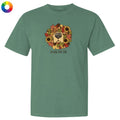A sage green short-sleeve t-shirt with a graphic of a dog's face surrounded by autumn leaves and sunflowers, with the text 'smells like fall' underneath. A small multicolor color wheel icon is in the top-left corner.