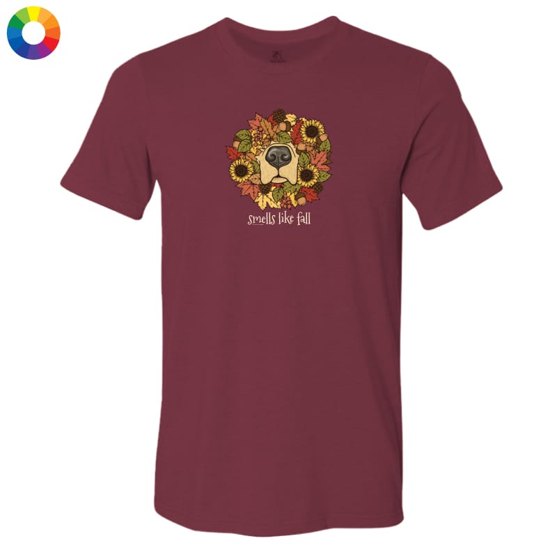 A maroon short-sleeve crewneck t-shirt featuring a graphic of a dog's face surrounded by autumn leaves and sunflowers, with the text 'smells like fall' printed below. A small multicolor color wheel icon is visible in the top-left corner.
