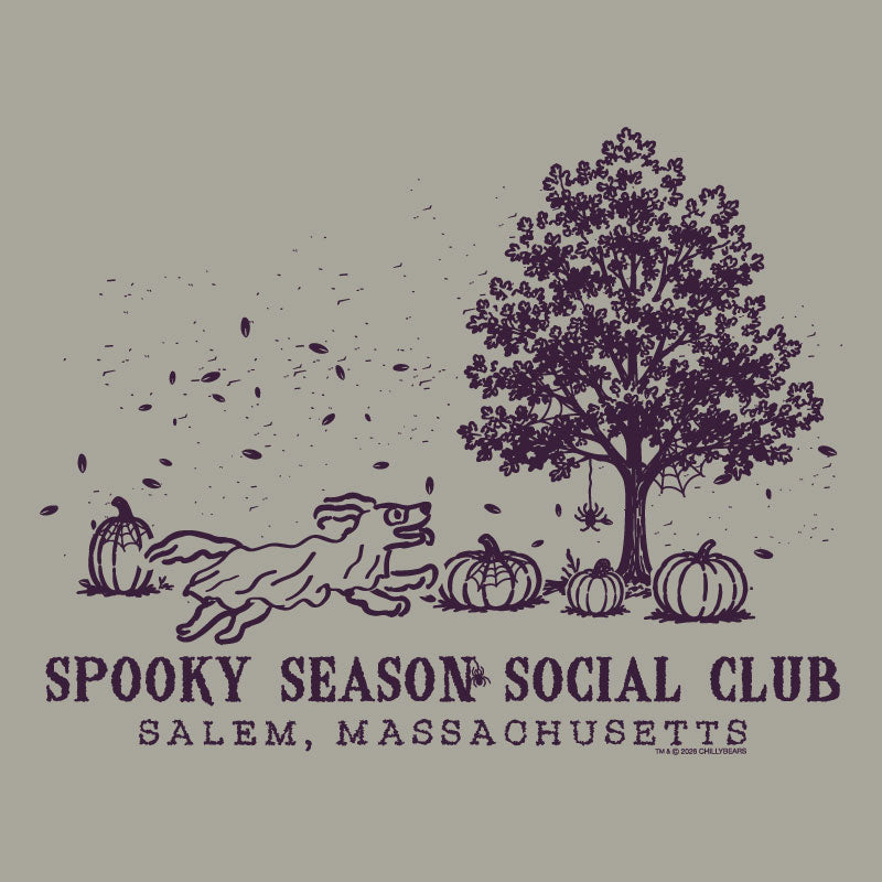 A vintage-style autumn graphic on a warm gray background, featuring a dark purple illustration of a tree, pumpkins, falling leaves, and a running dog. Text below reads 'SPOOKY SEASON SOCIAL CLUB' and 'SALEM, MASSACHUSETTS.