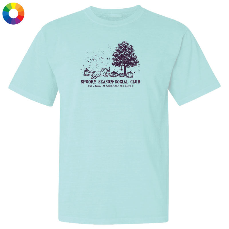 A light aqua blue short-sleeve t-shirt with a dark purple graphic on the chest depicting a tree, pumpkins, and the text 'SPOOKY SEASON SOCIAL CLUB' and 'PALM. NAPA, CA'.