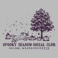 A peach-colored graphic print featuring a dark purple illustration of a running dog, pumpkins, a tree, and falling leaves, with the text 'SPOOKY SEASON SOCIAL CLUB' and 'SALEM, MASSACHUSETTS' below.