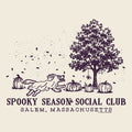 A vintage-style illustrated graphic on a warm cream background featuring a dark plum line drawing of a tree, pumpkins, falling leaves, and a running dog. Text below reads 'SPOOKY SEASON SOCIAL CLUB' and 'SALEM, MASSACHUSETTS.