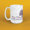 A white ceramic mug with a purple and gray autumn-themed graphic featuring pumpkins, a tree, a dog, and the text 'SPOOKY SEASON SOCIAL' and 'SALEM, MASSACHUSETTS', shown on a solid yellow background.