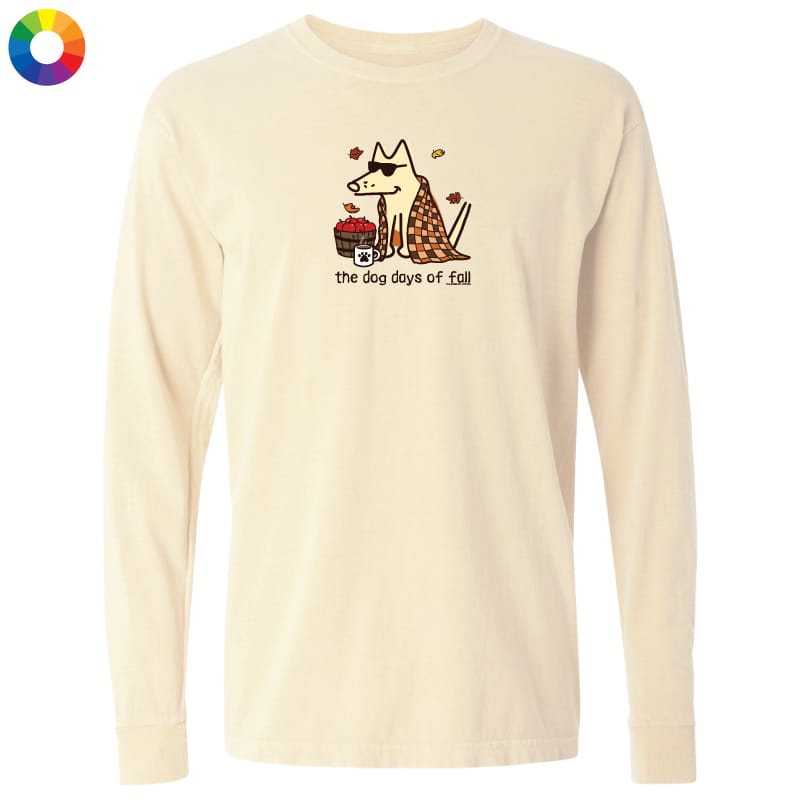 A cream-colored long-sleeve t-shirt with a graphic of a dog wearing sunglasses and a plaid sweater next to a hotdog, with the text 'the dog days of fall' printed below. A small multicolor color wheel icon is in the top-left corner.
