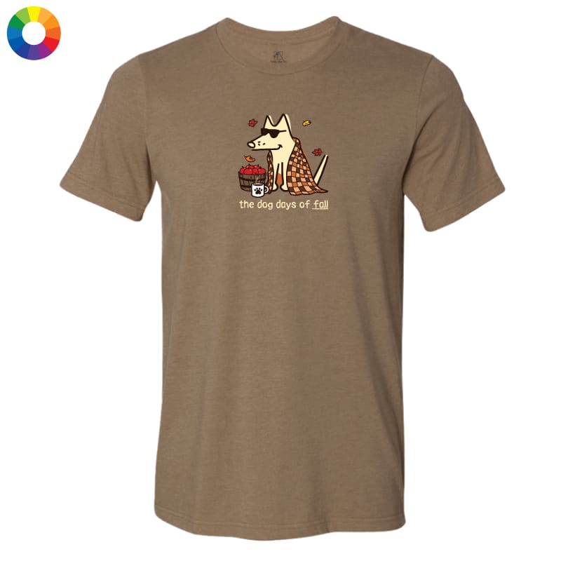 A heather brown short-sleeve t-shirt with a cartoon graphic of a dog wearing a plaid blanket and holding a basket of red apples, with the text 'the dog days of fall' printed below. A small circular color wheel icon is in the top-left corner.