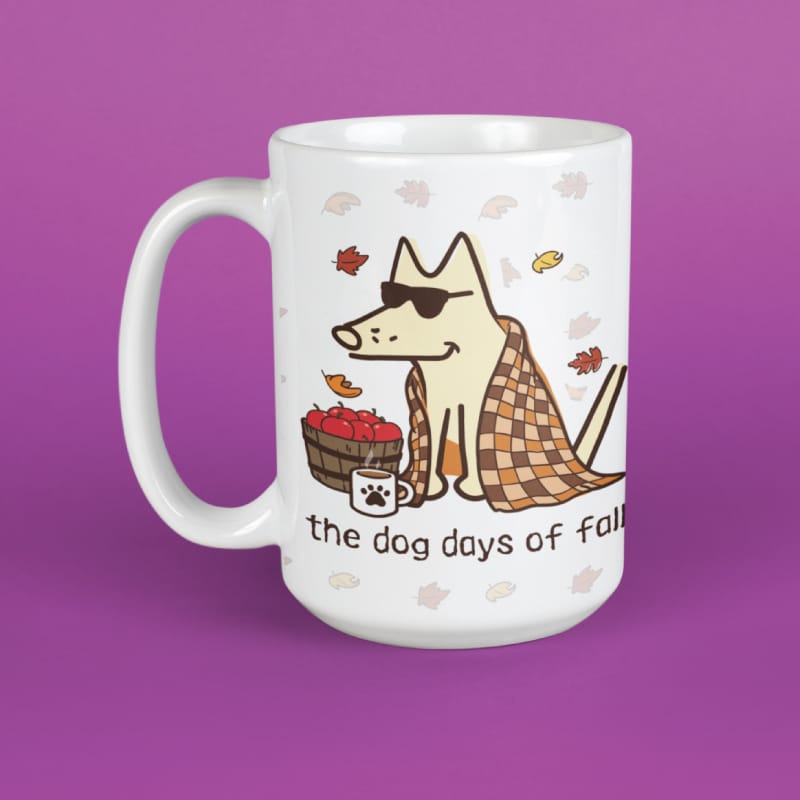 A white ceramic mug featuring a cartoon illustration of a dog wearing sunglasses and a plaid blanket, sitting next to a basket of red apples with the text 'the dog days of fall' on a solid purple background.