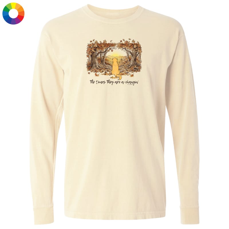 A cream-colored long-sleeve t-shirt with a central graphic of a yellow dog sitting in a forest of trees with autumn leaves, and the text 'The trees they see are a dreamer' underneath. A multicolor color wheel icon is in the top-left corner.