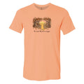 A peach-colored short-sleeve t-shirt with a graphic of a yellow dog standing in a glowing forest at night, with the text 'The dogs they are a family' printed below.