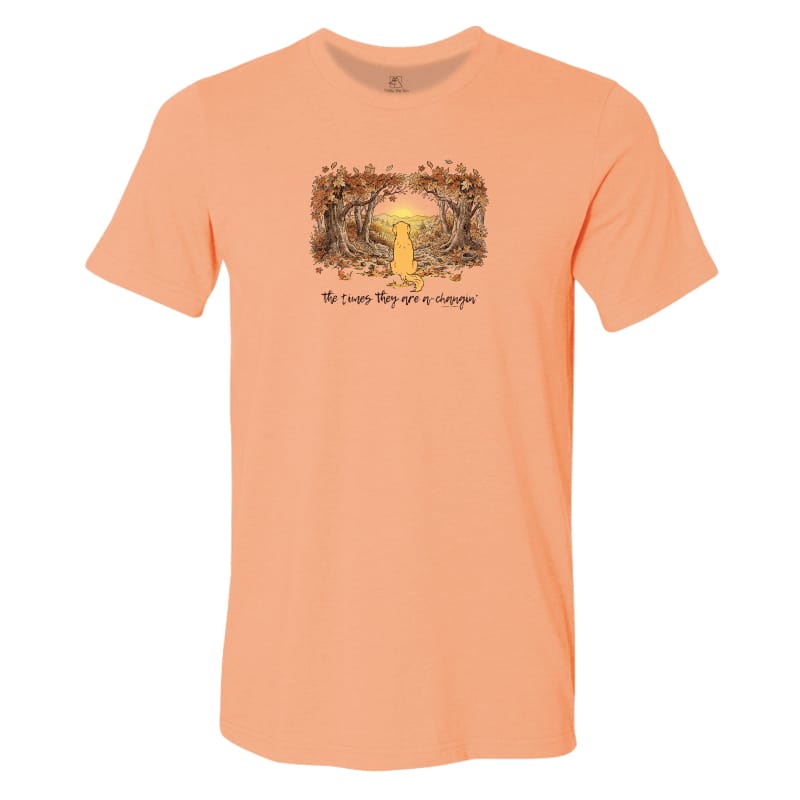A peach-colored short-sleeve t-shirt with a graphic of a yellow dog standing in a glowing forest at night, with the text 'The dogs they are a family' printed below.