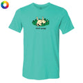 A turquoise short-sleeve crewneck t-shirt with a cartoon graphic of a cat lying on green grass and the text 'touch grass' printed below it. A small multicolor color wheel icon is visible in the top-left corner.